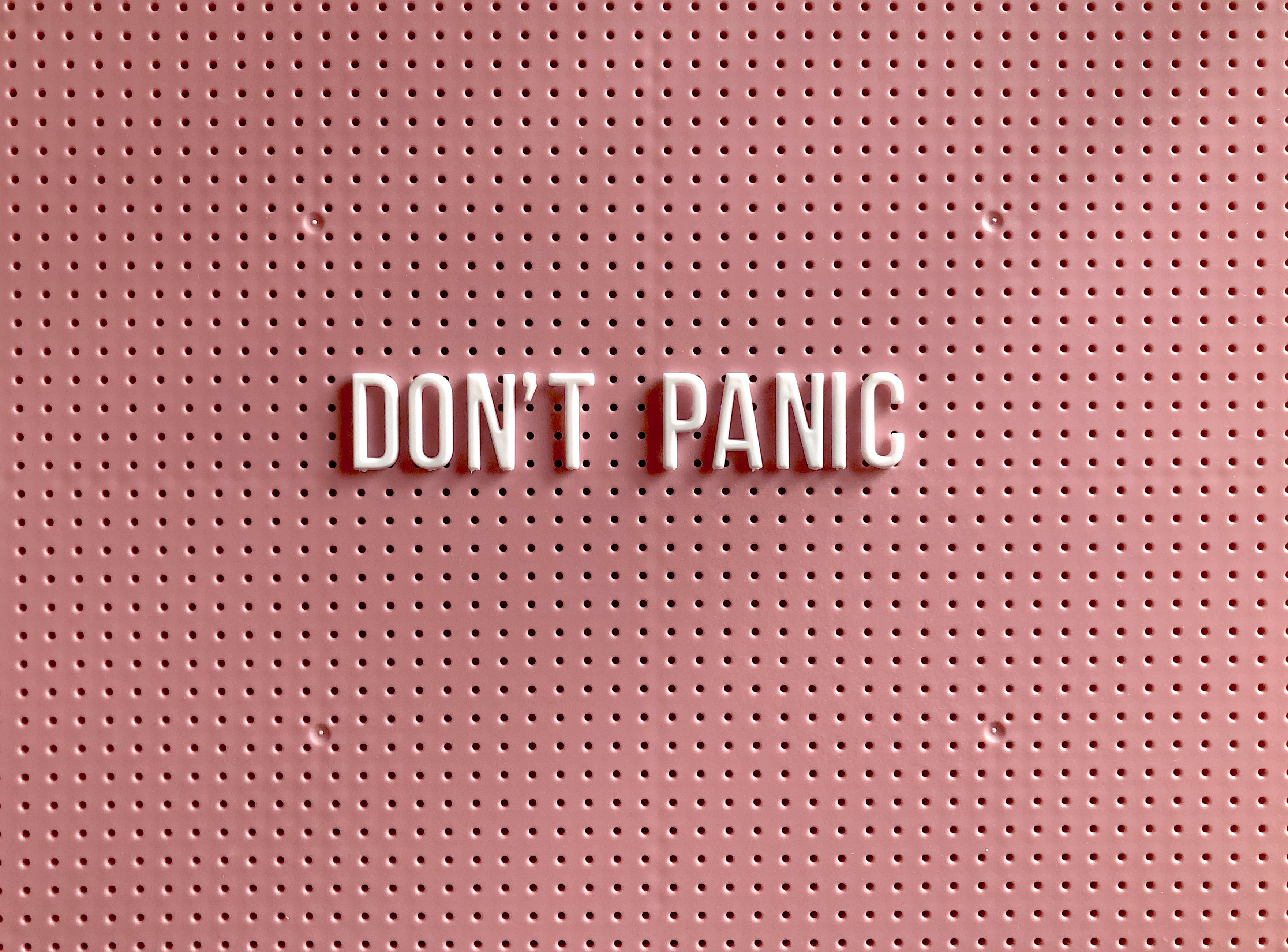A pink peg board with white letters pegged into it spelling Don't Panic  